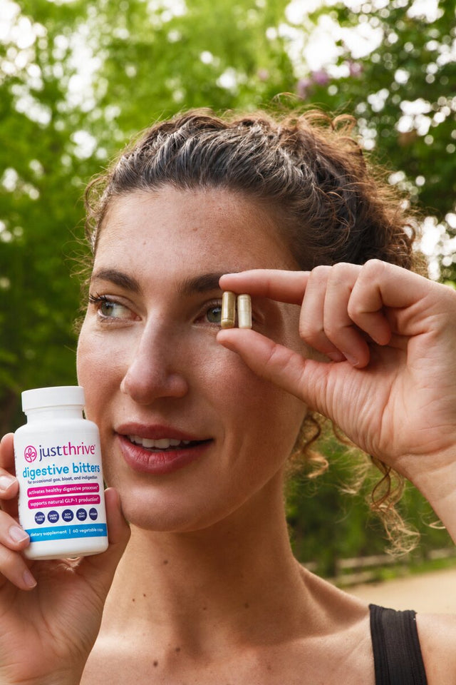 Woman holding two Digestive Bitters capsules and bottle
