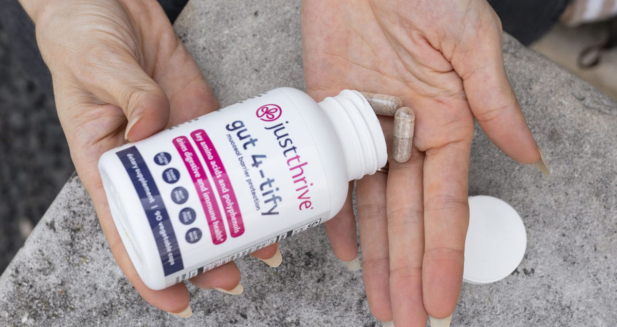 Hands holding an open bottle of Just Thrive Gut 4-tify with capsules in the palm