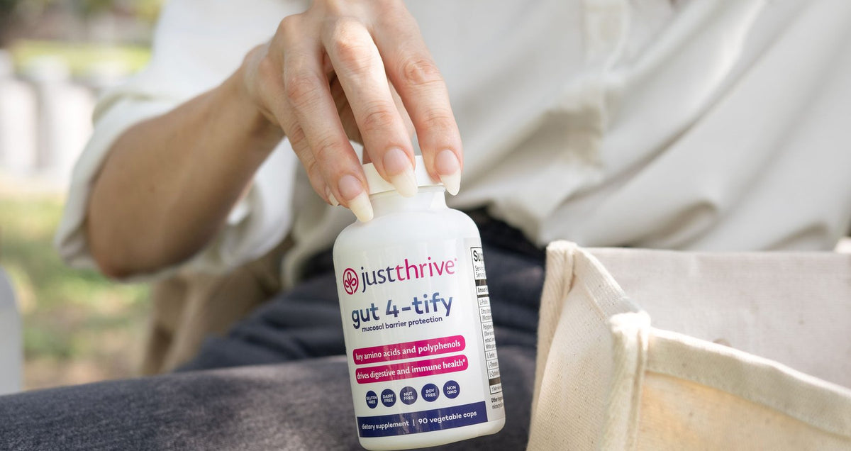 A hand placing a bottle of Just Thrive Gut 4-tify into a canvas tote bag
