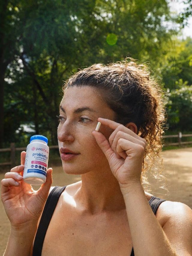 Woman holding a Just Thrive Probiotic capsule and bottle
